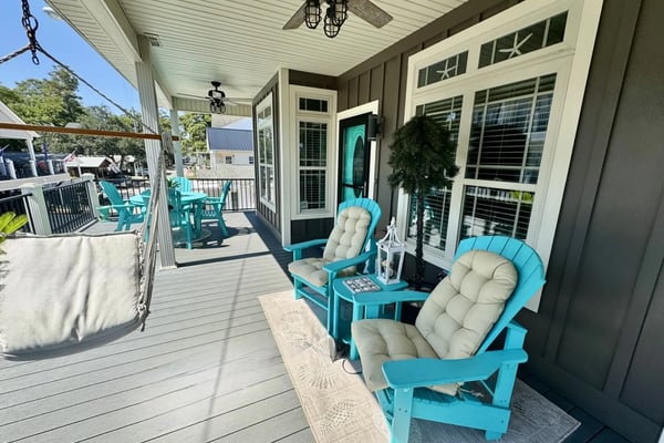 Open-plan beach house with mint-green kitchen, blue sofa, armchair, surfboards on wall, and ceiling fan.
