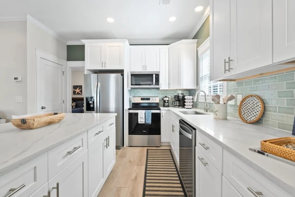 Open-plan kitchen and living room with white cabinetry, stainless steel appliances, island with bar seating, and waterfront view through glass doors.